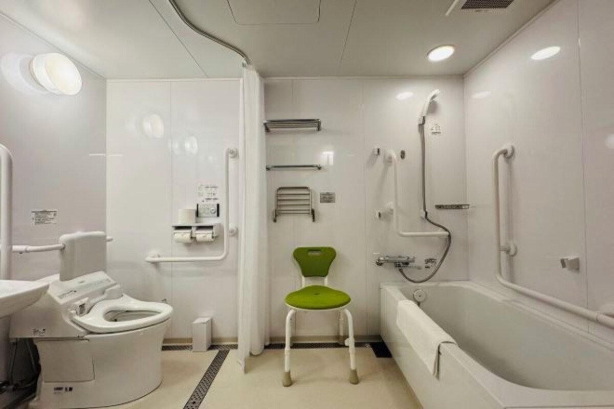 A modern bathroom with a toilet, a green chair, a bathtub, and a shower.
