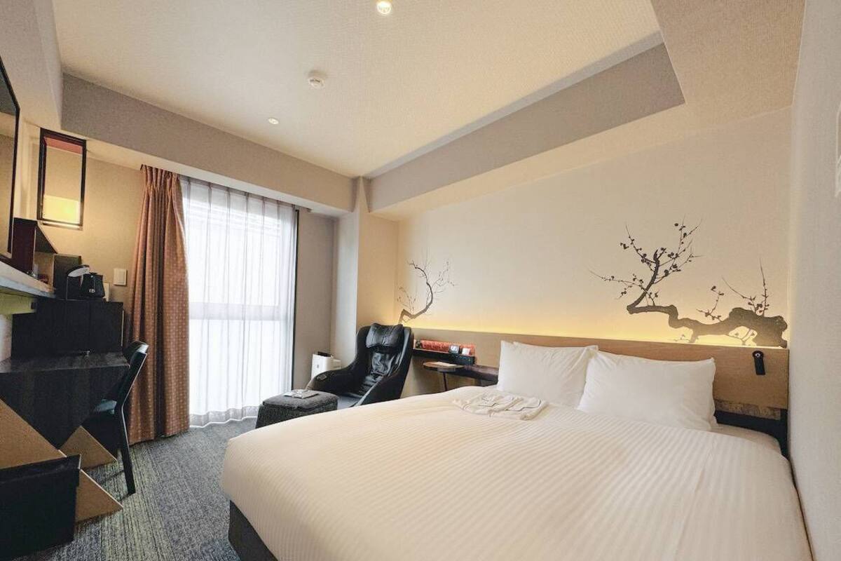 Ein Hotelzimmer mit Bett, Schreibtisch, Sessel, Nachttisch und einem Wandbild.