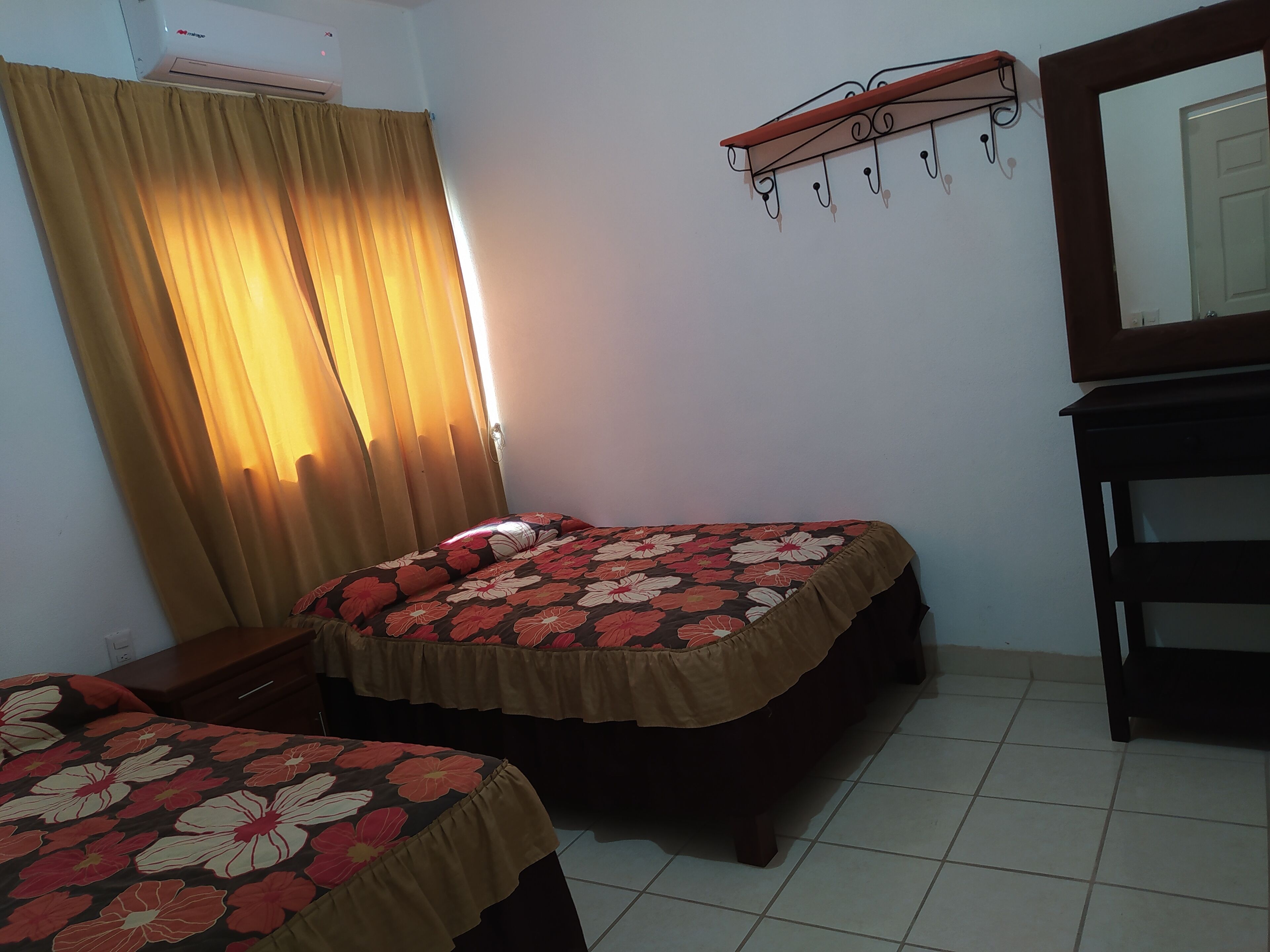 Un dormitorio con dos camas, un aparador de madera, un espejo y una estantería en la pared.