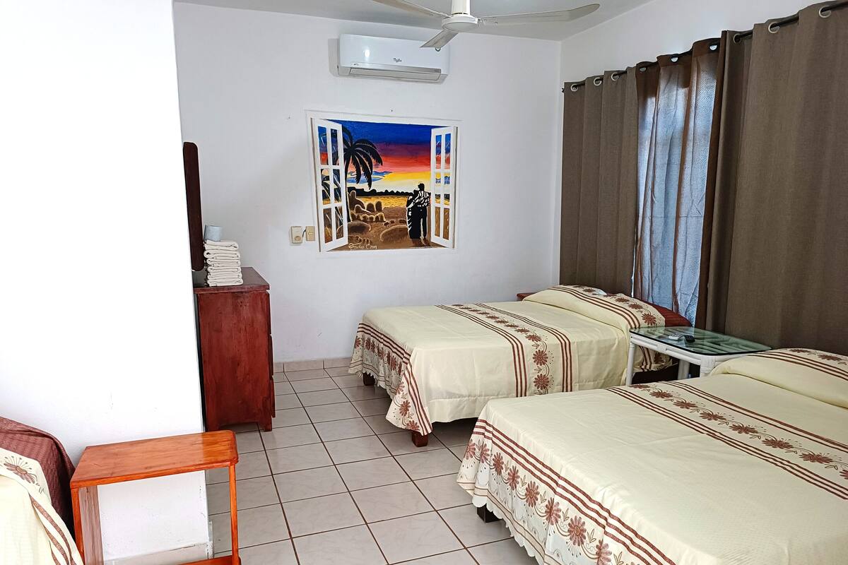 Ein Hotelzimmer mit zwei Betten, einem Schreibtisch, einem Stuhl, einem Fenster mit Vorhängen und einem Bild an der Wand.
