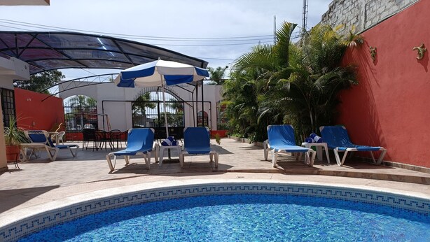 A swimming pool with blue mosaic tiles, surrounded by lounge chairs and a covered seating area. - Hotel Lulu (Tondoroque)