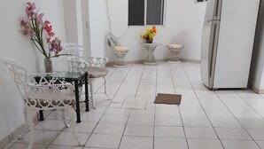 A spacious kitchen with white tiled flooring, a dining area with white chairs and a glass table, and a refrigerator. - Hotel Lulu (Tondoroque)