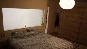A bedroom with a bed, a window, a hanging light fixture, and a wardrobe. - Casa Nina (Ostend)