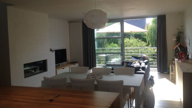 A modern living room with a dining area, large windows, and a view of greenery. - Casa Nina (Ostend)