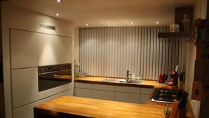 A modern kitchen with a wooden countertop, stainless steel appliances, and a window with vertical blinds. - Casa Nina (Ostend)