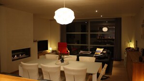 A modern living room with a dining area, a fireplace, and a large window. - Casa Nina (Ostend)