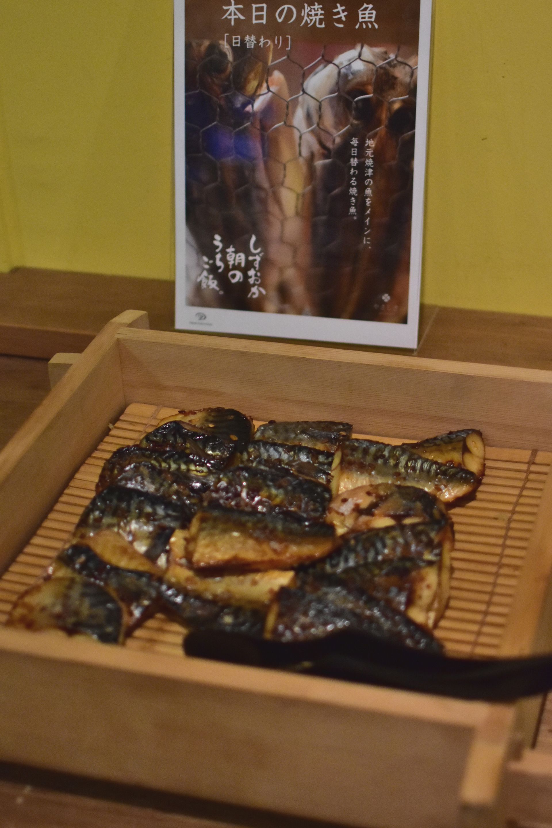 A wooden box containing grilled fish, with a poster in the background.