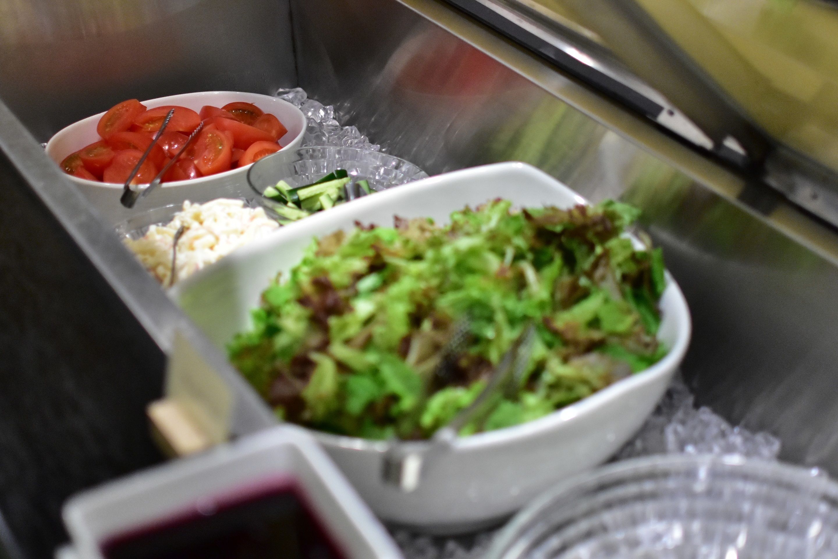 A stainless steel buffet setup with various food items including a bowl of sliced tomatoes, a bowl of green salad, and a container of rice.