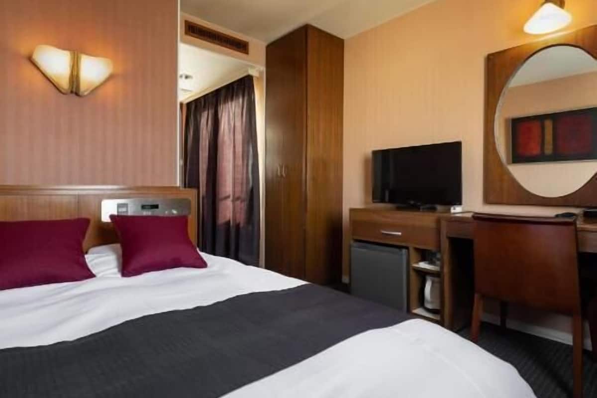 A hotel room with a bed, a desk, a television, and a mirror.