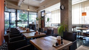 A restaurant interior with high ceilings, exposed ductwork, and large windows offering views of the outdoors. Tables are set with candles and salt shakers. - Fujieda Park in Hotel (Fujieda)