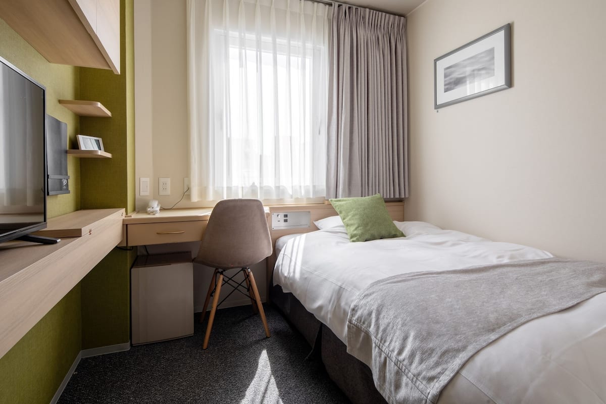 A hotel room with a bed, a desk, a chair, a TV, and a window with curtains.