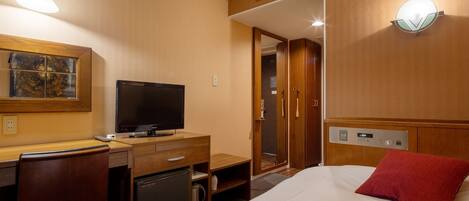 A hotel room with a bed, a desk with a television, a small refrigerator, and a shower area.