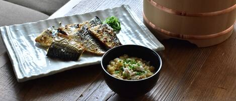 Un plato de pescado a la parrilla y un bol de arroz con cebolletas sobre una mesa de madera.