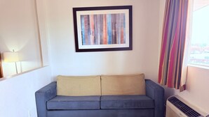 Une pièce avec un canapé bleu, un tableau abstrait encadré, une table basse en bois et une fenêtre avec des rideaux.