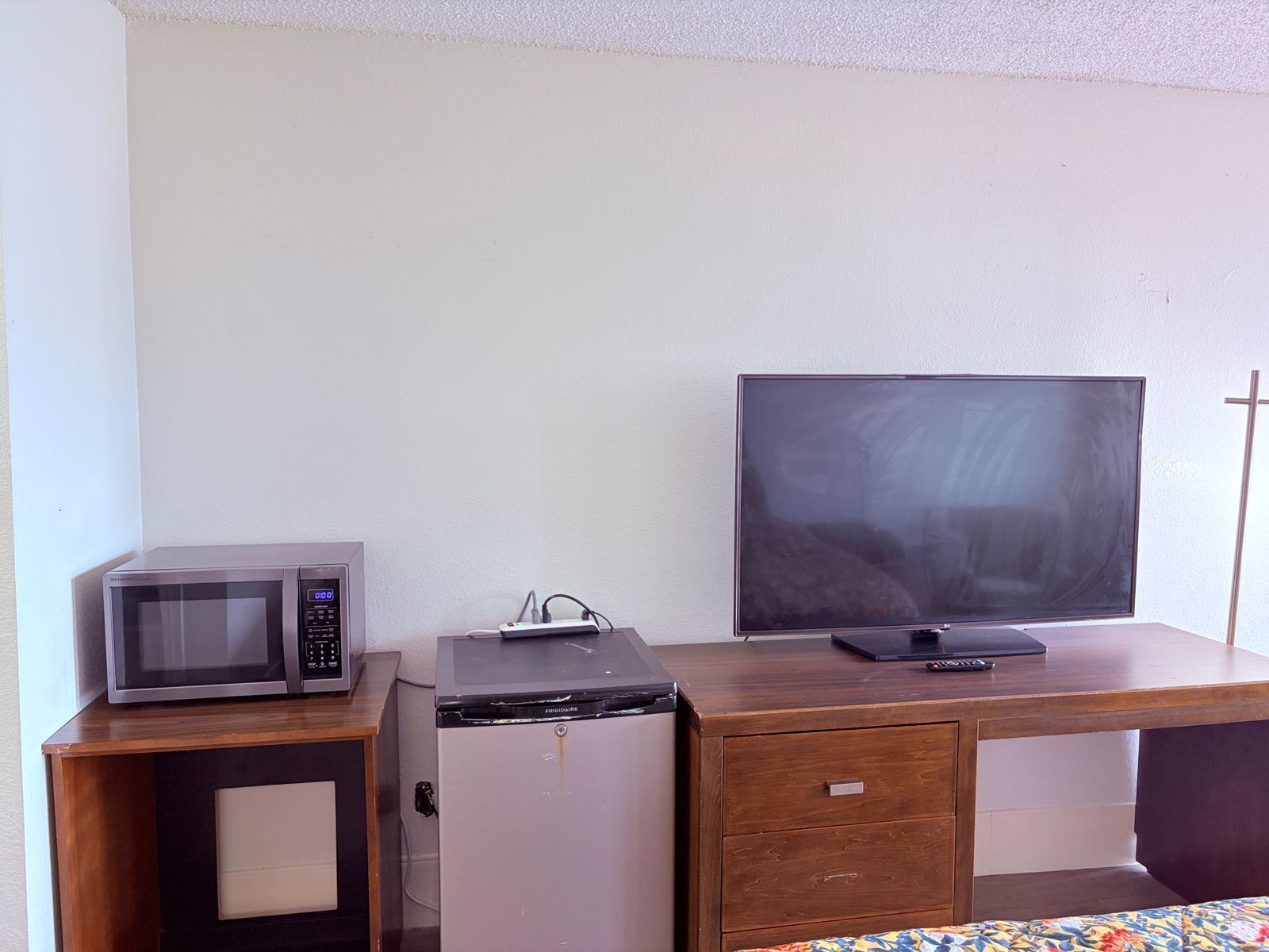 Une petite cuisine équipée d’un four à micro-ondes, d’un petit réfrigérateur et d’un téléviseur à écran plat posé sur un bureau en bois.