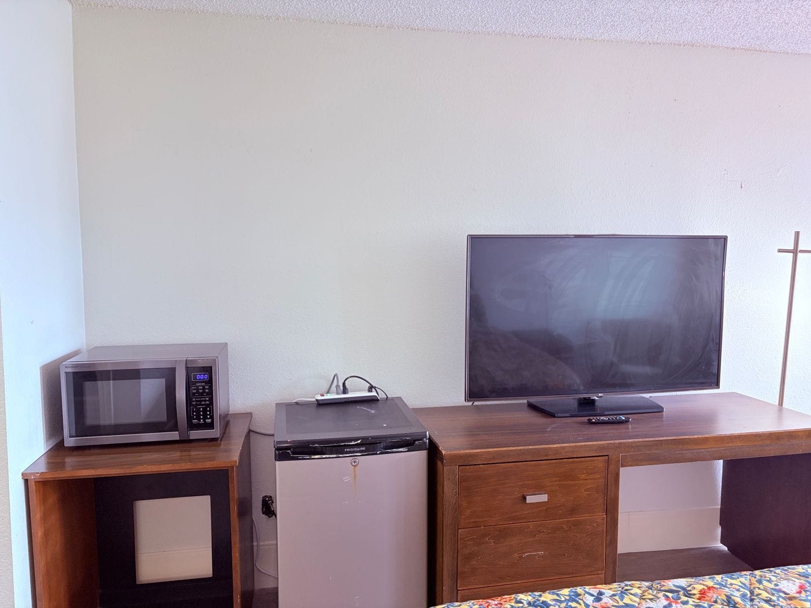 A room with a wooden desk, a flat-screen TV, a microwave, and a mini-fridge.