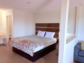 Een slaapkamer met een bed, een houten hoofdbord, witte kussens en een beddegoed met een patroon.