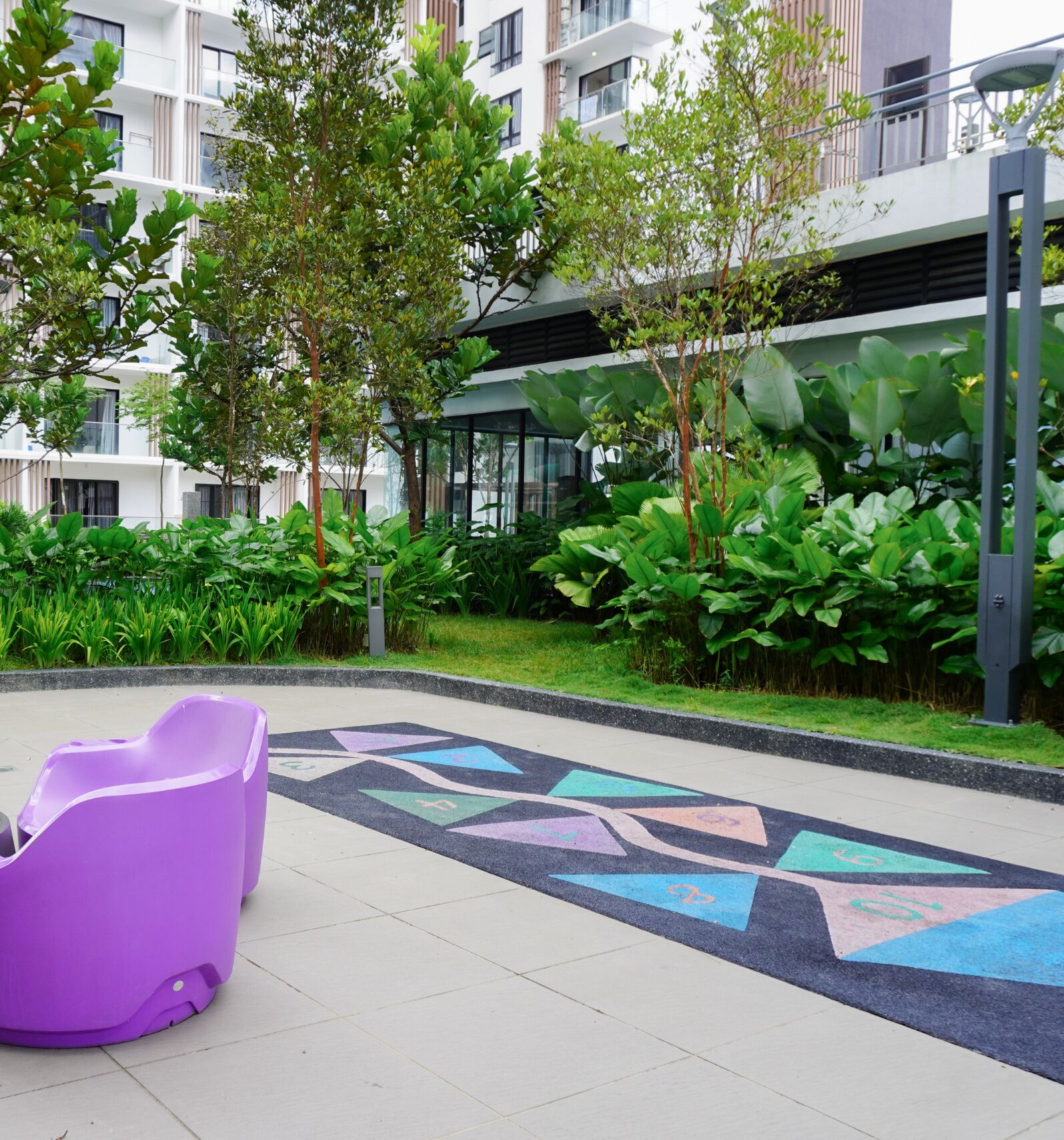 A modern outdoor area with a purple seating area, lush greenery, and a patterned floor.