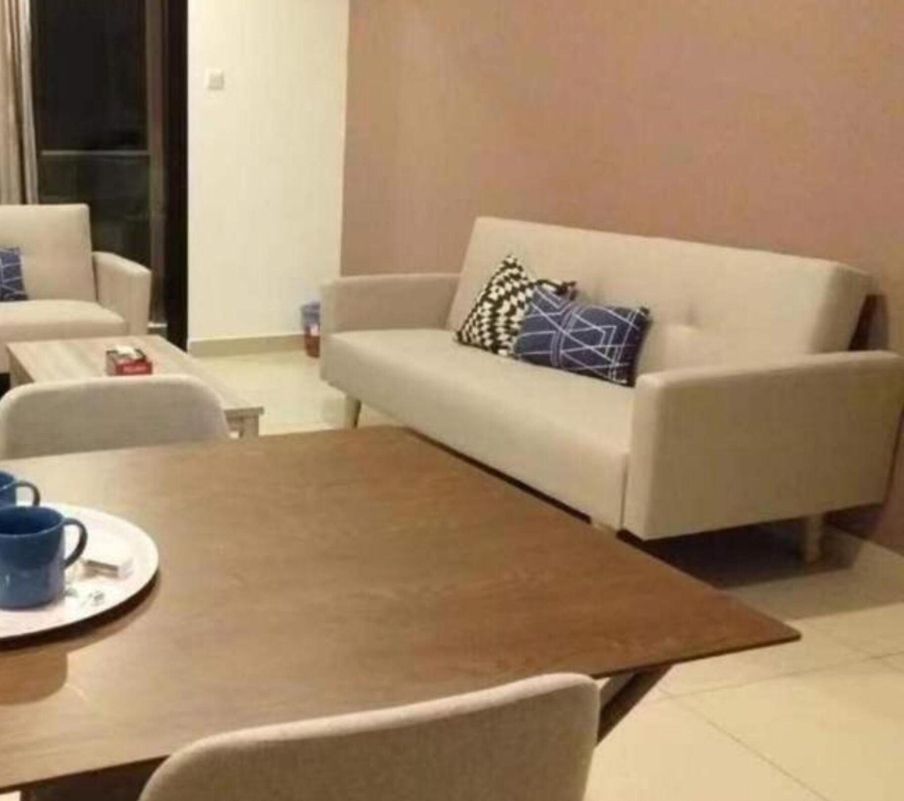 Un salón con un sofá color beige, una mesa de centro y una taza azul sobre un platito.