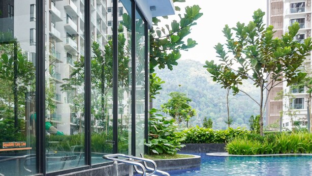 A modern indoor swimming pool with clear glass walls, surrounded by lush greenery and tall residential buildings. - 7Stonez Suites Midhills Genting Highlands (Genting Highlands)