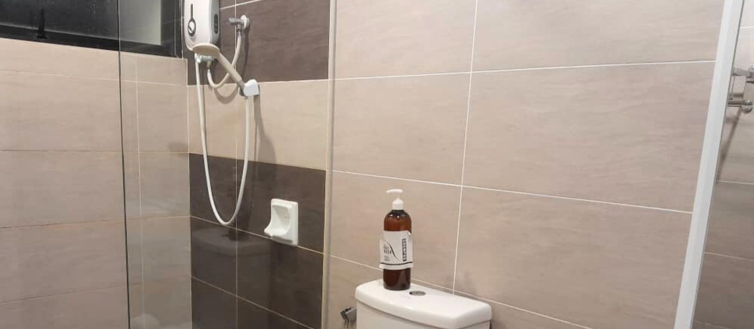 A bathroom with a glass shower enclosure, a toilet, and a bottle of hand sanitizer on the toilet.