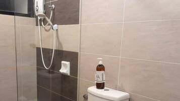 A bathroom with a glass shower enclosure, a toilet, and a bottle of hand sanitizer on the toilet.