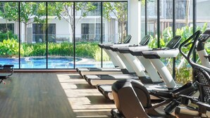 A gym with exercise equipment, large windows, and a view of a swimming pool and greenery. - 7Stonez Suites Midhills Genting Highlands (Genting Highlands)