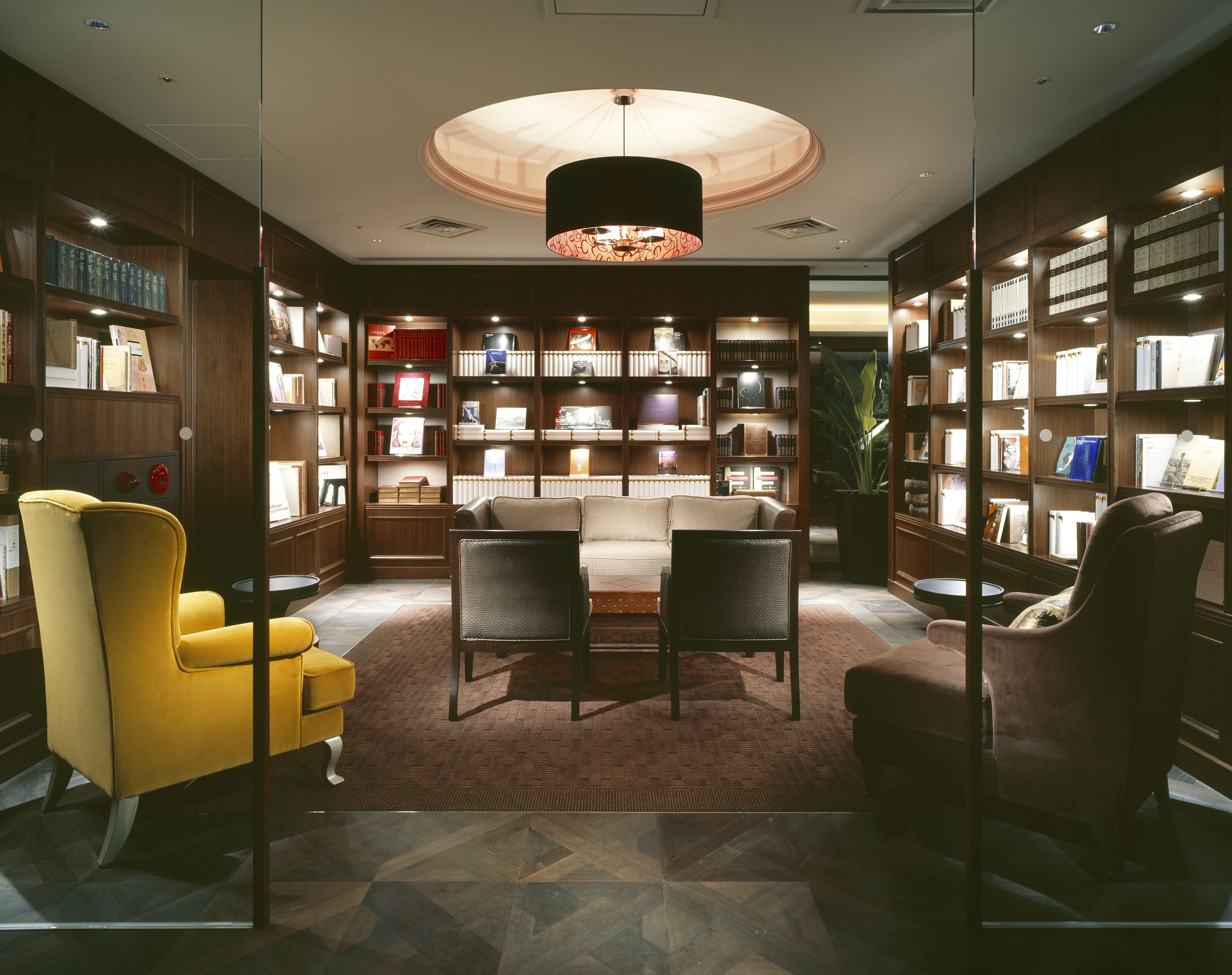 A library with bookshelves, a sofa, and a yellow armchair.