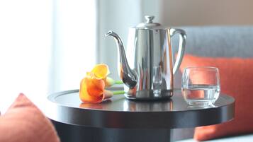 A small round table with a silver teapot, a glass of water, and a single orange flower.