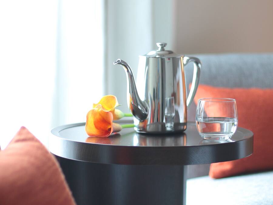 A small round table with a silver teapot, a glass of water, and a single orange flower.