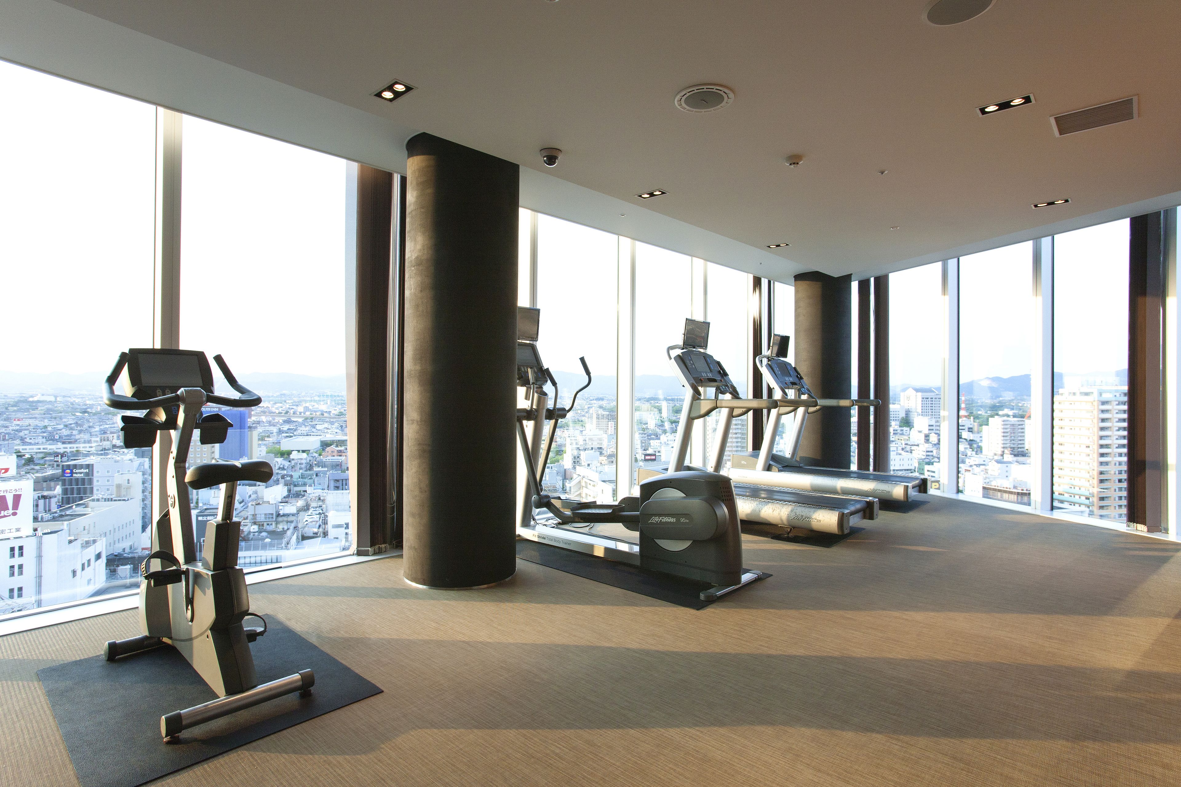 A gym with cardio machines, large windows, and a city view.