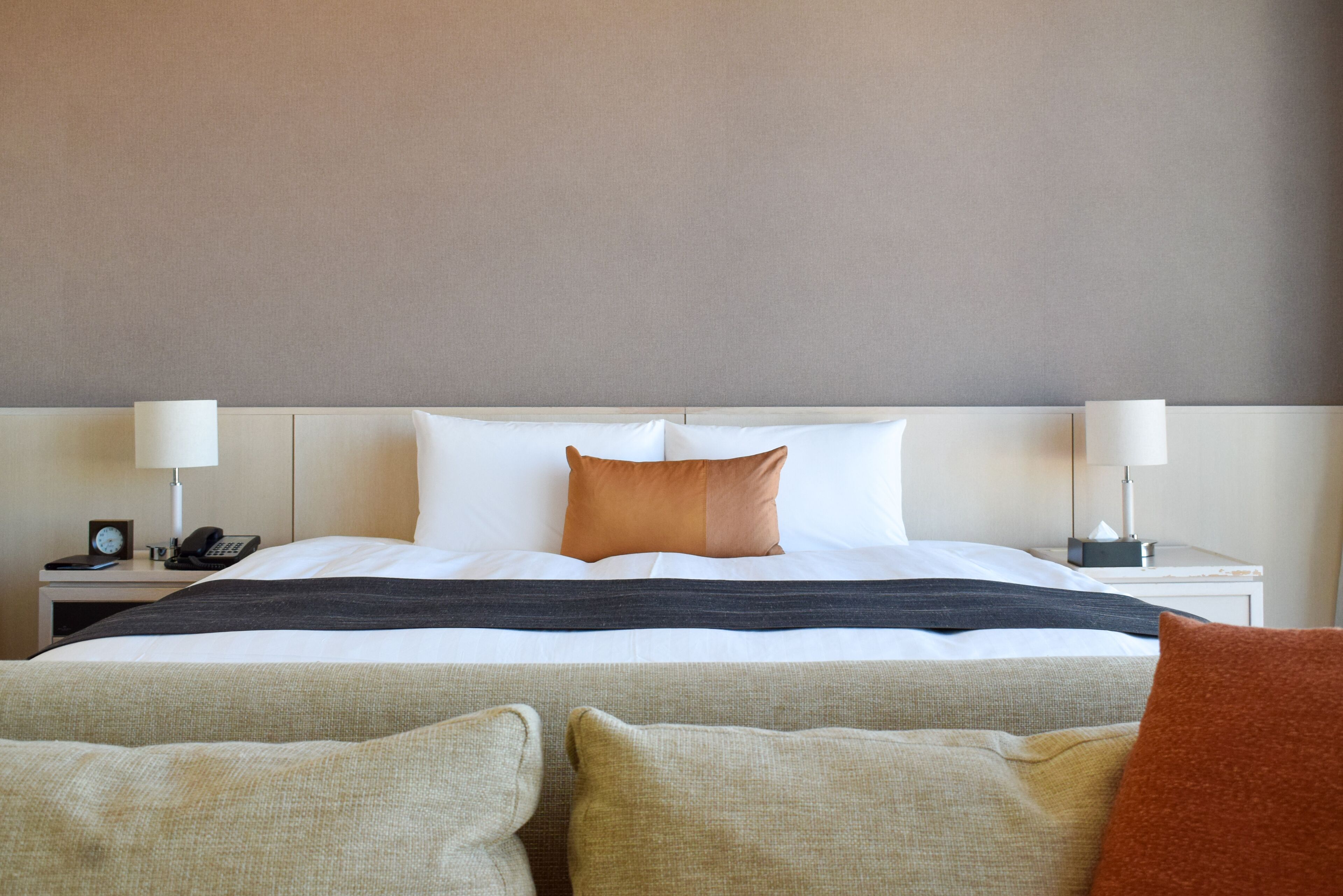Una habitación de hotel con una cama bien hecha, dos mesitas de noche con lámparas y un reloj en una de ellas.