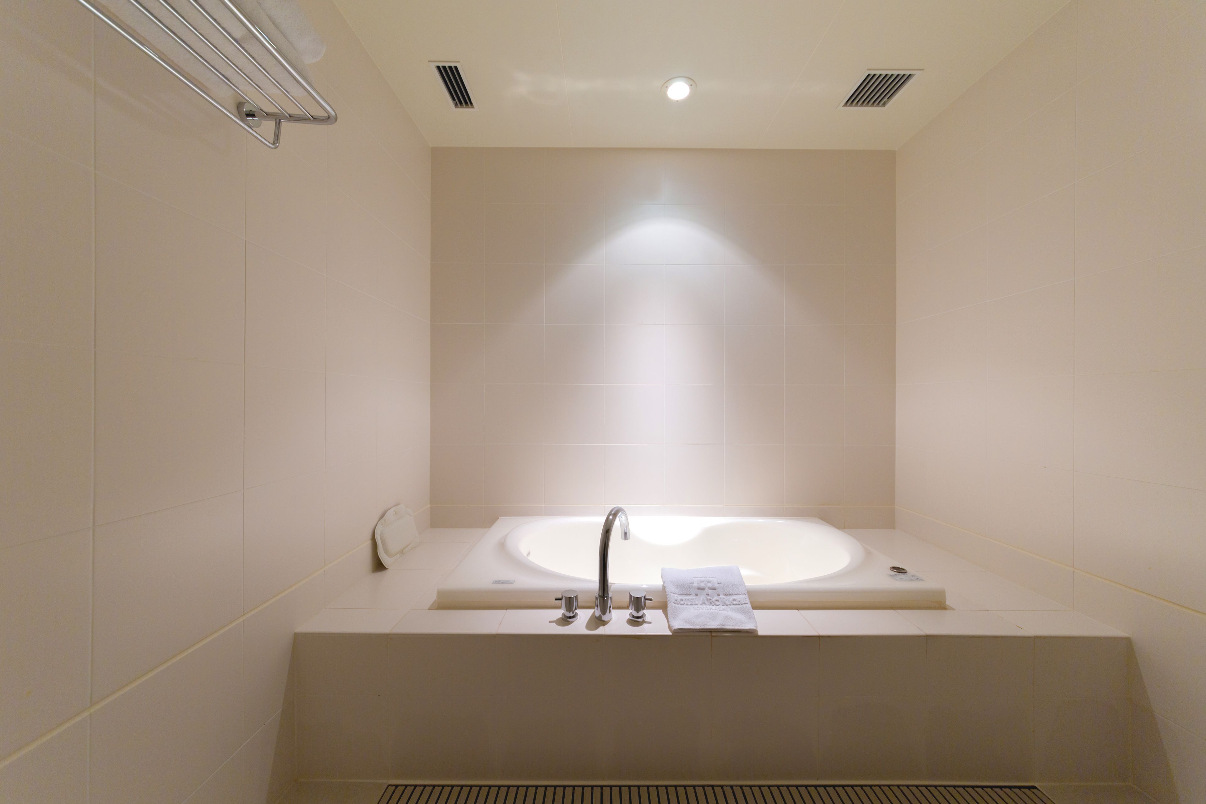 A modern bathroom with a large bathtub, a towel rack, and a vent on the ceiling.