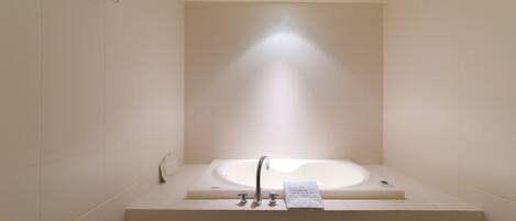 A modern bathroom with a large bathtub, a towel rack, and a vent on the ceiling.