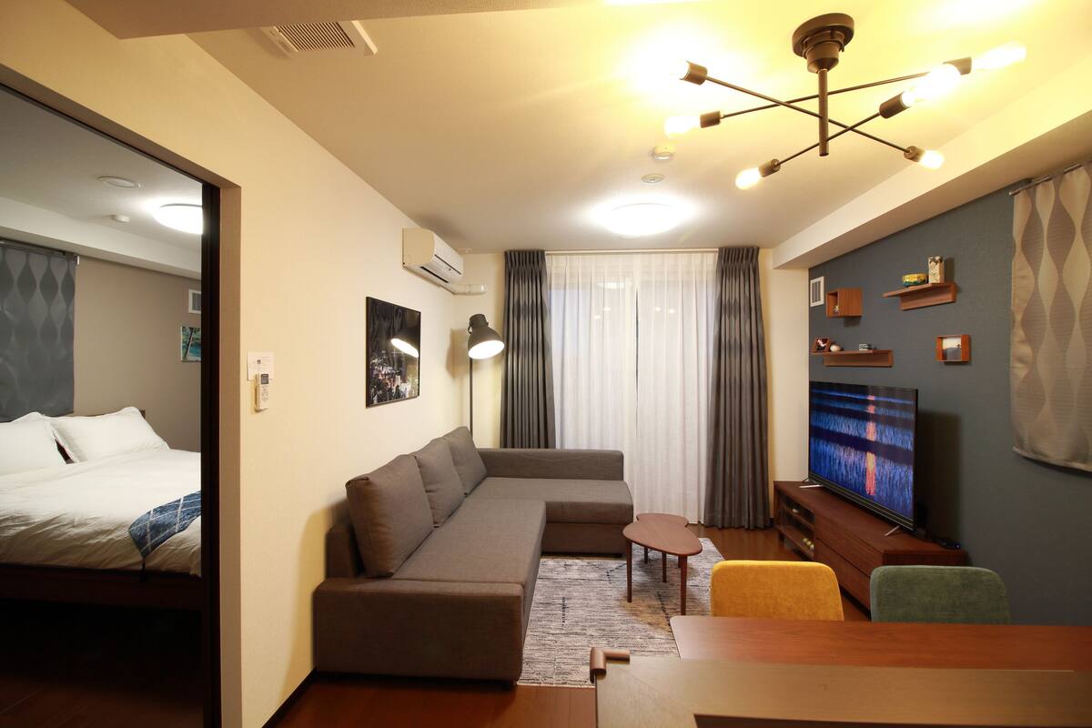 A modern hotel room with a large bed, a sofa, a small table, a TV, and a ceiling light fixture.