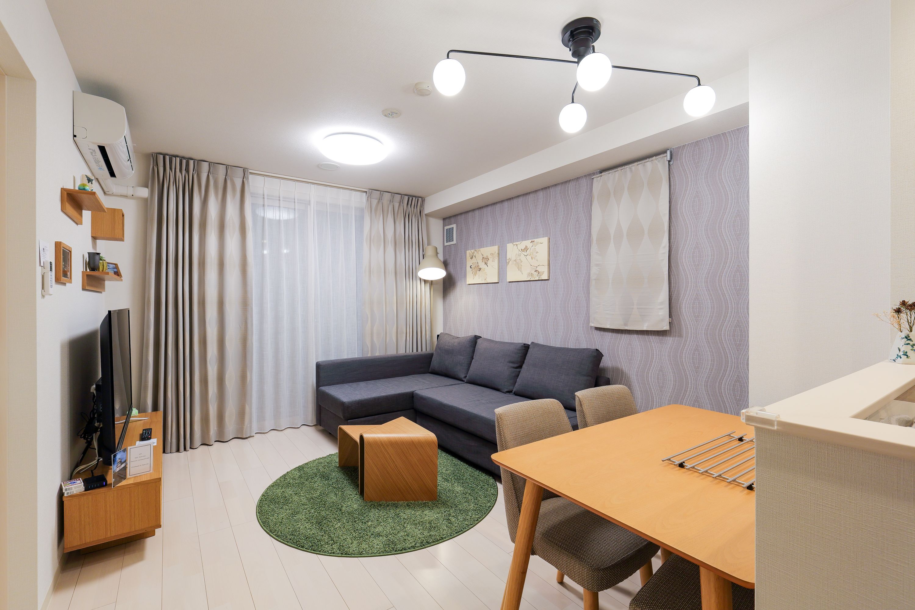 A modern living room with a sectional sofa, a wooden coffee table, a dining table, and a green rug.