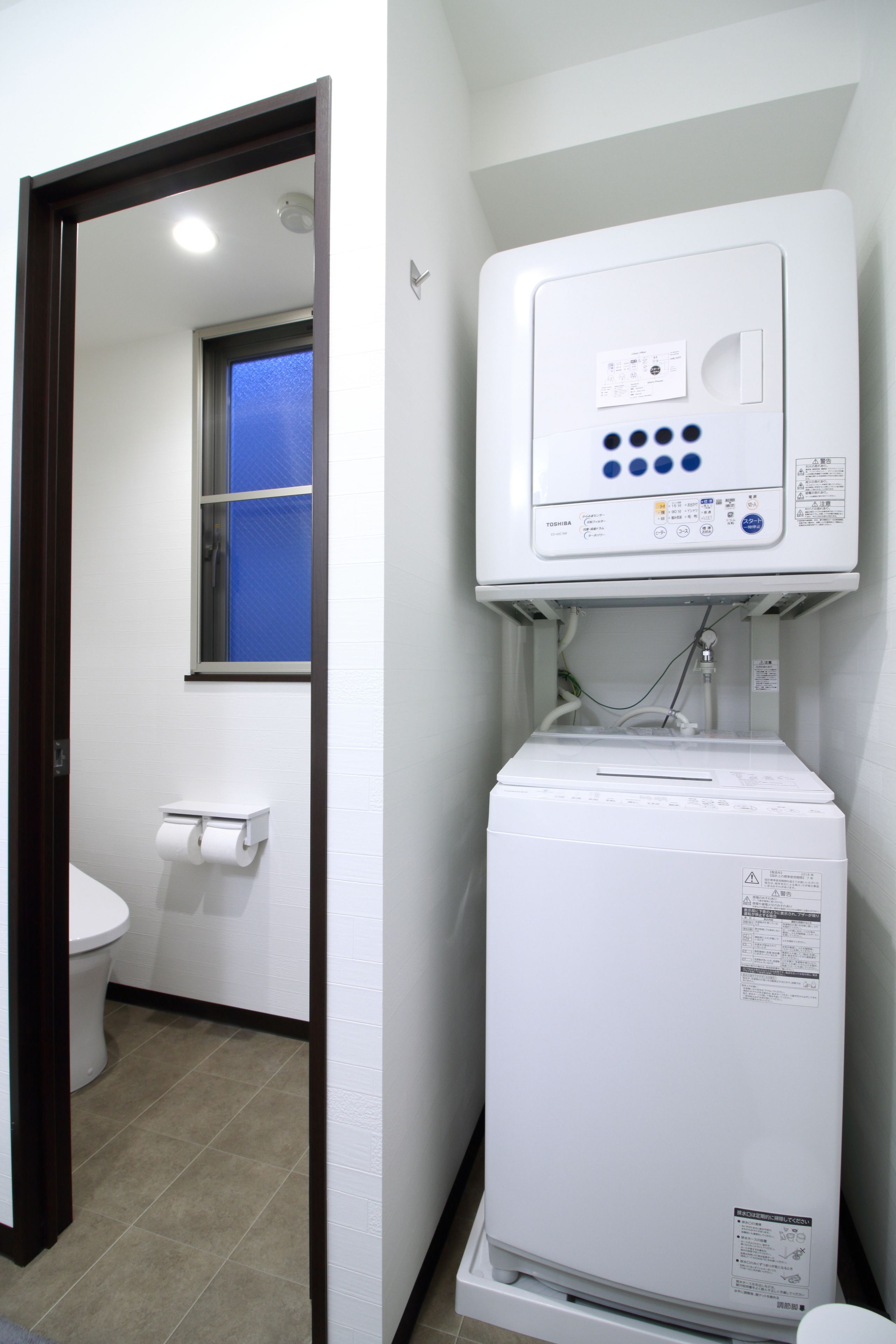 A compact bathroom with a toilet, a towel dispenser, and a white water heater unit.