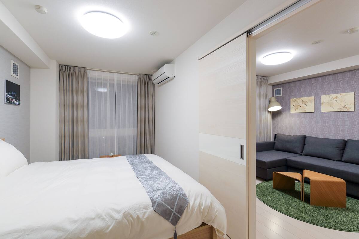 A modern hotel room with a bed, a sofa, a small table, and a green rug.