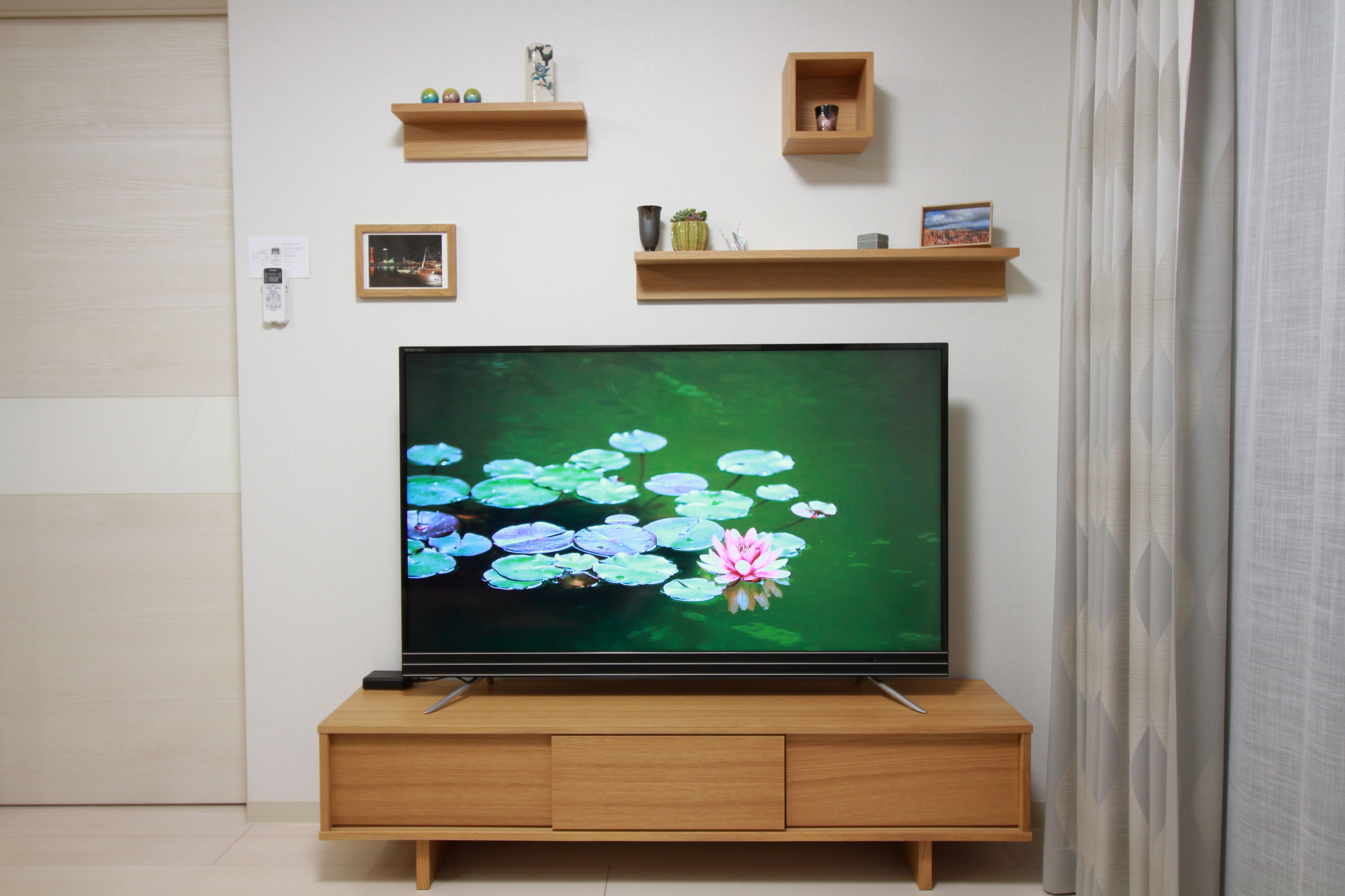 Un téléviseur posé sur un meuble en bois, avec une étagère fixée au mur au-dessus.