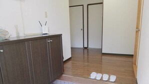 A hallway with a wooden floor, a tiled area, and a set of white shoes on the floor.