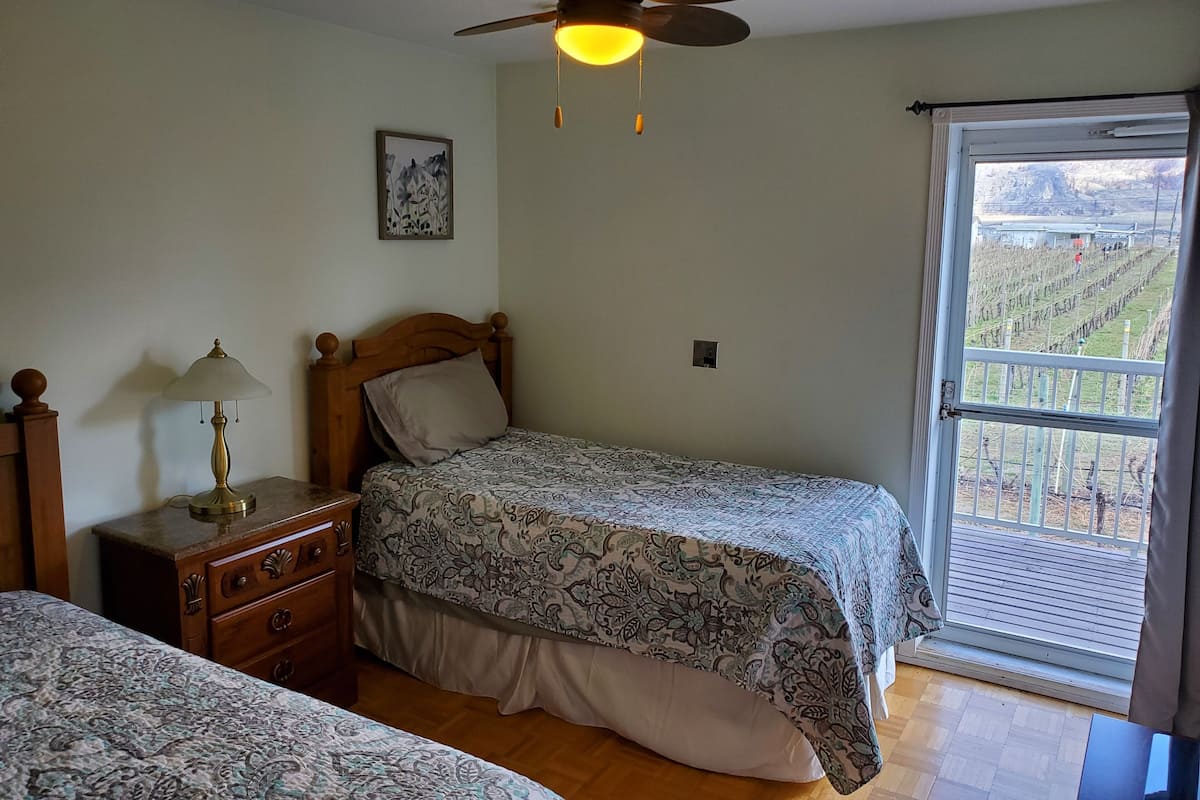 Une chambre à coucher avec un lit, une table de chevet avec une lampe, un ventilateur de plafond et une fenêtre donnant sur un vignoble.