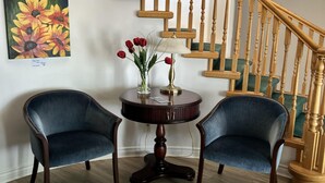 A staircase with wooden balusters and a handrail, a round wooden table with a vase of red roses and a lamp, and two blue armchairs in a room with wooden flooring. - Sonora Desert Inn (Osoyoos)