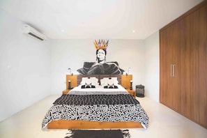 A bedroom with a large bed, a wooden wardrobe, and a wall-mounted air conditioner.