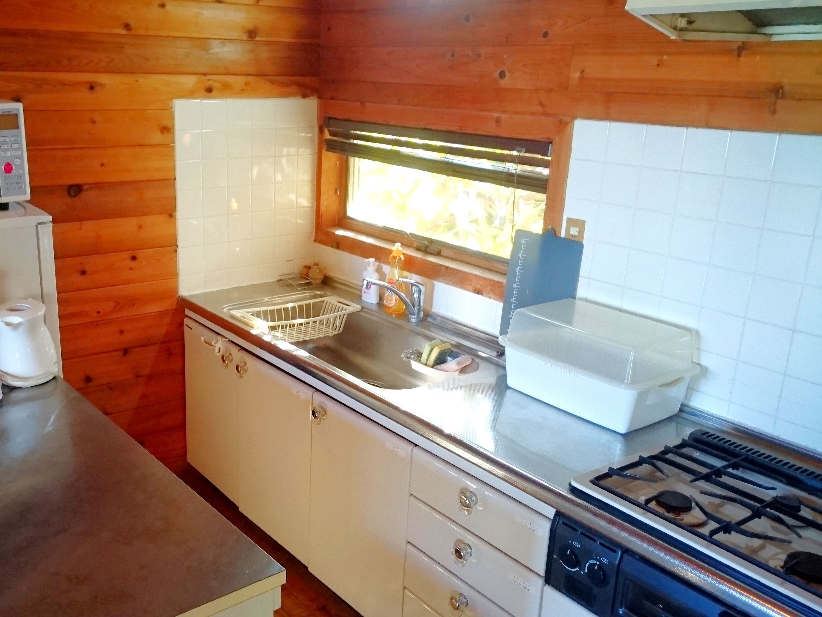 A compact kitchen with wooden walls, a stainless steel sink, a gas stove, and white cabinets.
