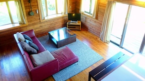 A cozy cabin interior with a sofa, a coffee table, and a TV. - Private Beach House (Motobu)