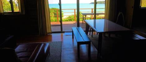 A room with a wooden floor, a bench, a table, and a view of the sea through large windows.