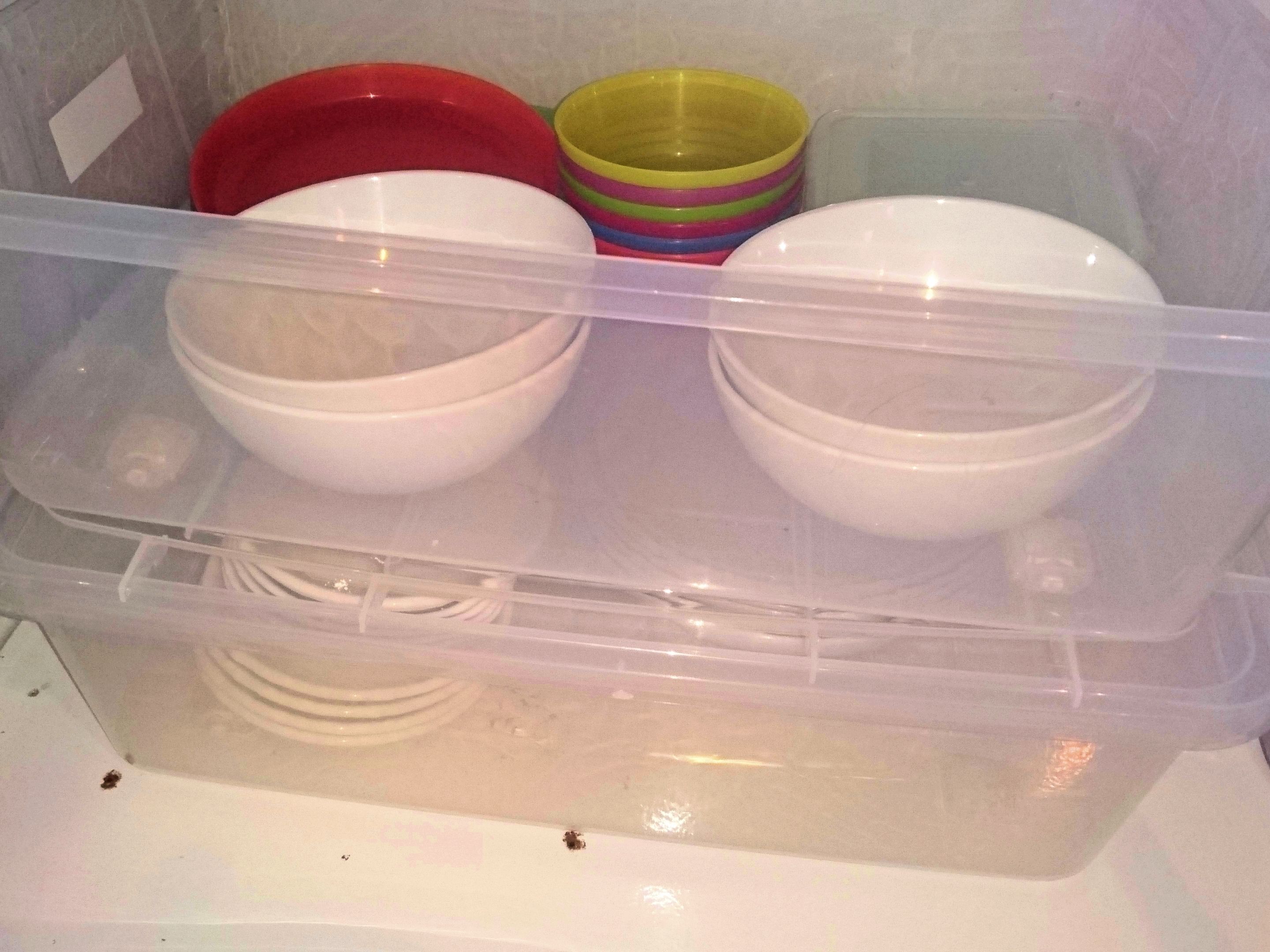 A storage container with white bowls and colorful plastic bowls.