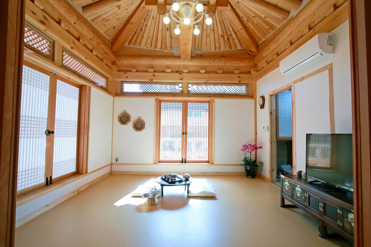 A traditional Japanese-style room with tatami flooring, sliding doors, a television, and a ceiling fan.