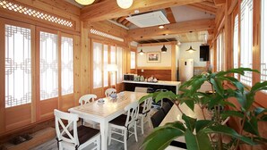A wooden interior with a dining table and chairs, a kitchen area, and large windows. - Wiyeonjae Hanok Stay (Gyeongju)