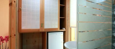 A compact room with wooden cabinets, a small refrigerator, and a glass partition.